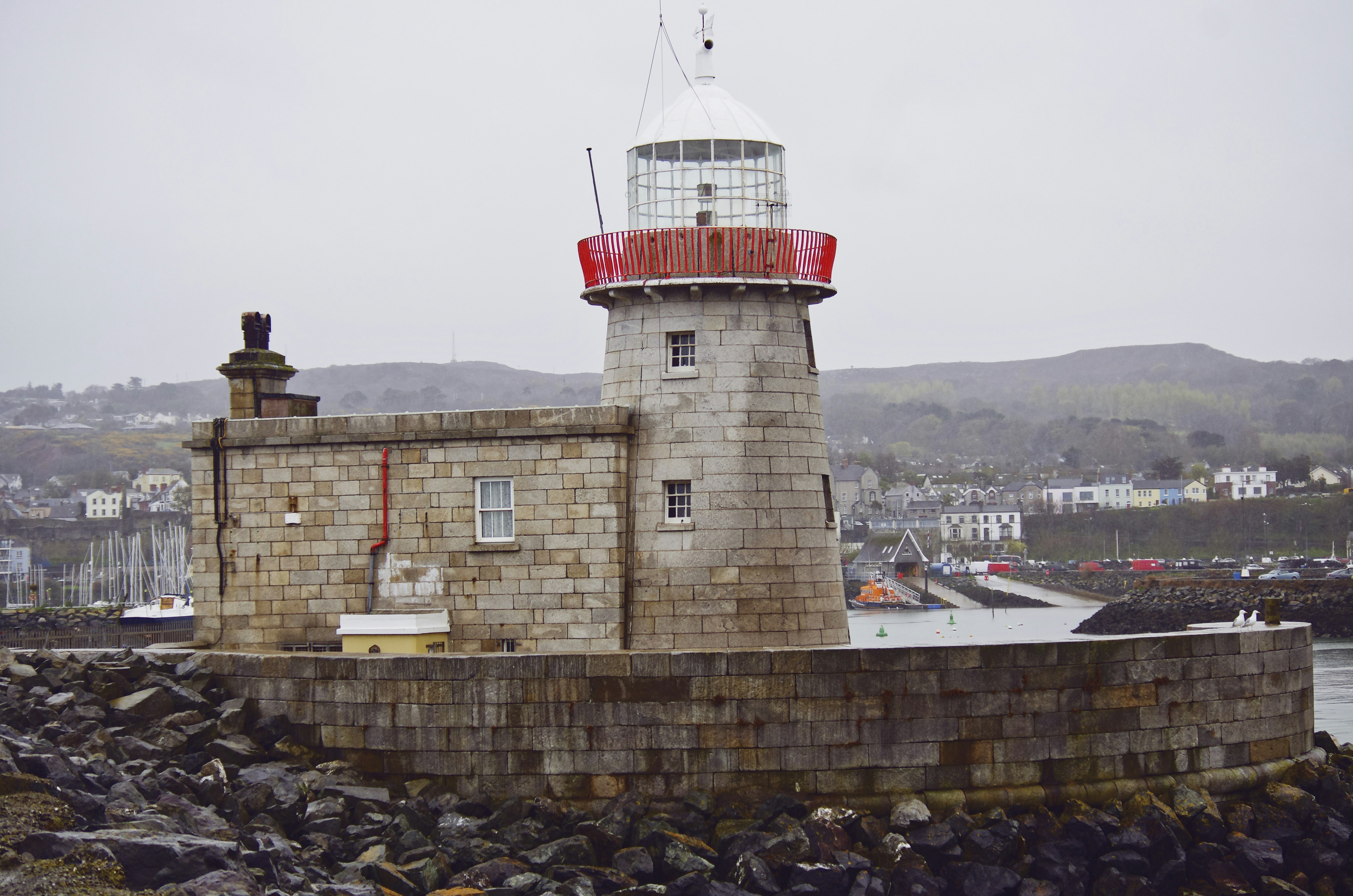 white and red concrete lighthouse near city buildings during daytime